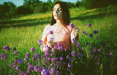 Young woman touching purple flowers on grassy field