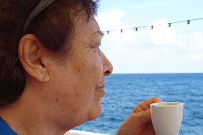 Portrait of mid adult woman holding coffee cup by sea