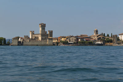 Sea by cityscape against clear blue sky