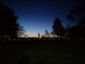 Silhouette trees on field against clear sky at night