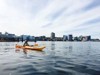 Woman kayaking in sea against cloudy sky