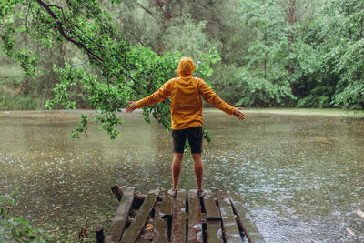 Rear view of boy standing by lake in forest