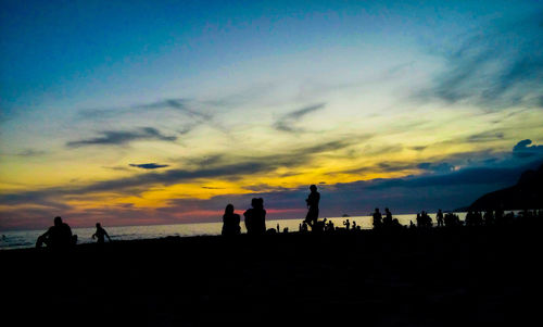 Silhouette people on beach against sky during sunset