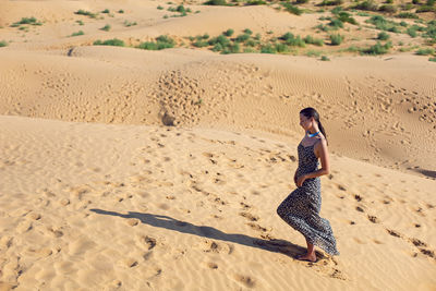 Brunette woman in a long leopard dress stands with her back in the desert at sunset. go everywhere