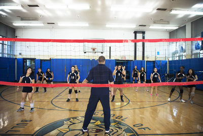 Male coach teaching exercise to female volleyball team