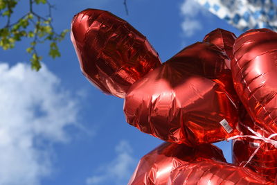 Low angle view of red helium balloons against sky