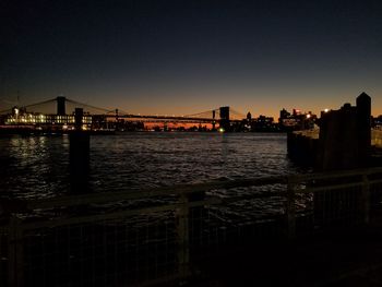 Illuminated bridge over river against sky at night