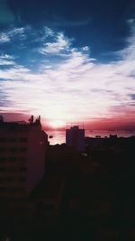 Silhouette city against dramatic sky during sunset