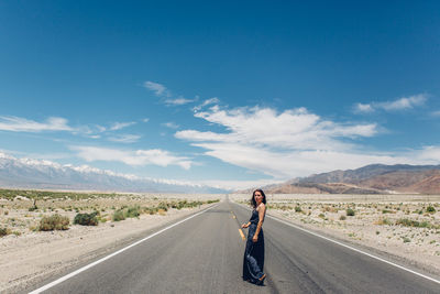 Woman walking on road at desert against blue sky