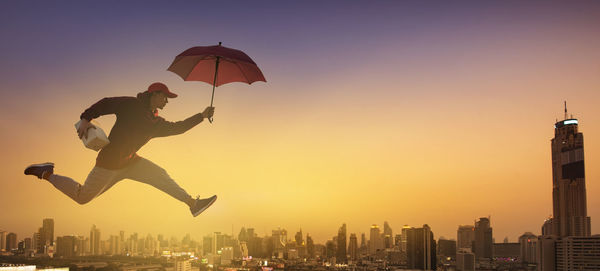 Low angle view of man jumping over buildings against sky during sunset