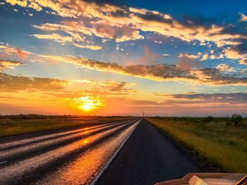 Road amidst field against sky during sunset