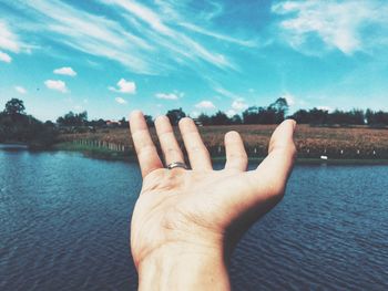 Close-up of hand by lake against sky