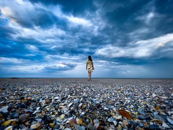 Person standing on pebbles on beach against sky