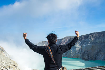 Rear view of man with arms outstretched standing against mountain