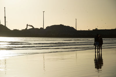 Silhouette people walking on beach against clear sky during sunset