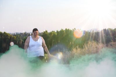 Overweight young woman standing against sky during sunny day