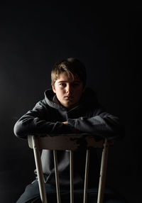 Low key portrait of adolescent boy sitting on a chair in a dark room.