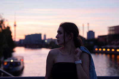 Thoughtful woman standing against river during sunset