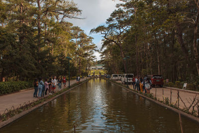 People walking on canal in city against sky