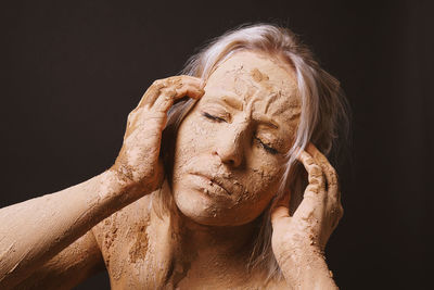 Close-up of woman with muddy face over black background