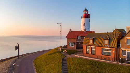 Lighthouse by sea against clear sky during sunset