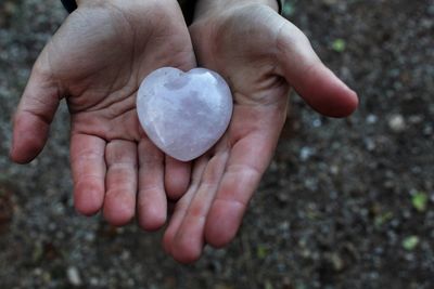 Cropped hands of woman holding heart shape stone outdoors