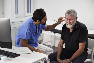 Male doctor examining senior patient's ear during appointment