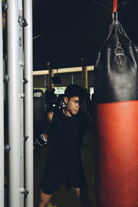 Young focused asian man training boxing performing punches while exercising with heavy punching bag in a modern gym