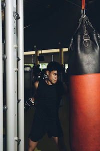 Young focused asian man training boxing performing punches while exercising with heavy punching bag in a modern gym