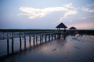 Pier on beach against sky during sunset