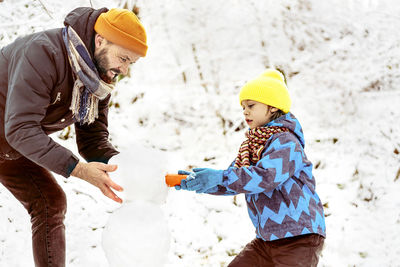 Joyful dad and son enjoying building a snowman.