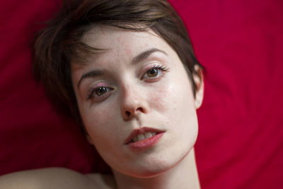 High angle portrait of young woman resting on pink bed