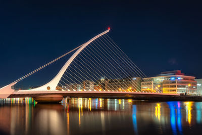 Harp shaped samuel beckett bridge with city lights reflected in liffey river, dublin