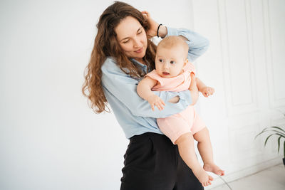 Young mother with long hair and in a shirt holds a newborn daughter. in the arms of a 6 month old 