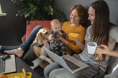 Happy family - grandmother, daughter, newborn baby and dog rest in the living room on the couch