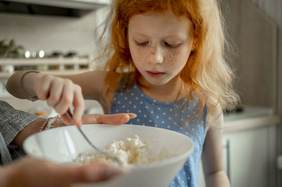 Redhead girl mixing cheese in bowl at home