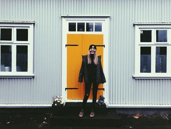 Portrait of young woman standing against window of building
