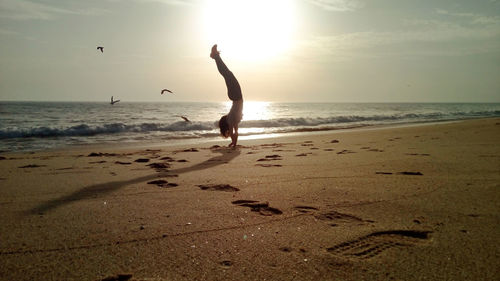 Woman performing handstand at beach against sky on sunny day