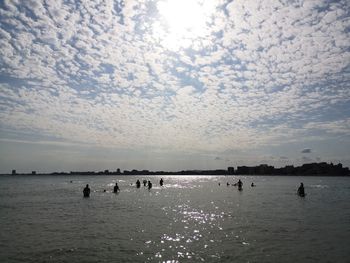 Silhouette people swimming in sea against sky