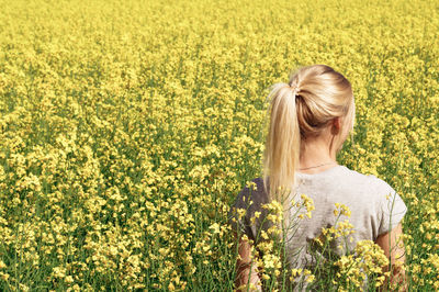 Rear view of young woman standing amidst oilseed rape