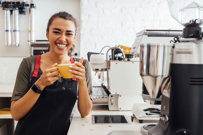 Portrait of smiling barista holding coffee at cafe