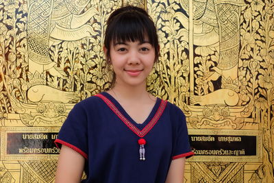 Portrait of young woman standing against mural at temple