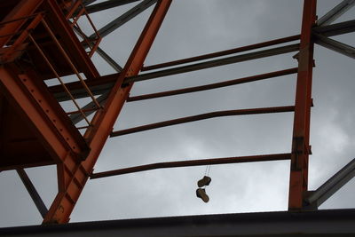 Low angle view of shoes hanging on metal structure against cloudy sky