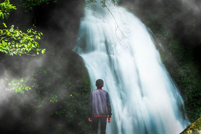 Rear view of man standing against waterfall