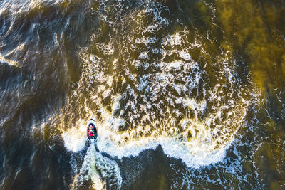 Aerial view of man rides on fast water scooter jumping on waves and making golden splashes on sunset
