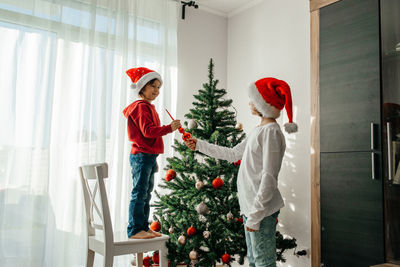 Children in red santa claus hats decorate the christmas tree for the holiday. eve of new year