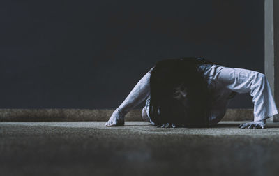 Spooky young woman crouching on floor against wall