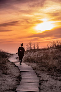 Rear view of silhouette man on footpath against sky during sunset