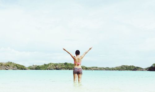 Rear view of woman with arms raised standing in sea