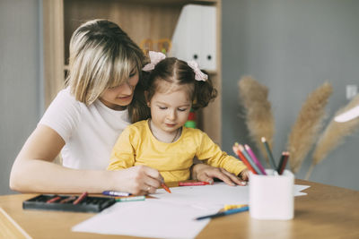 Mother and girl looking down while sitting on table